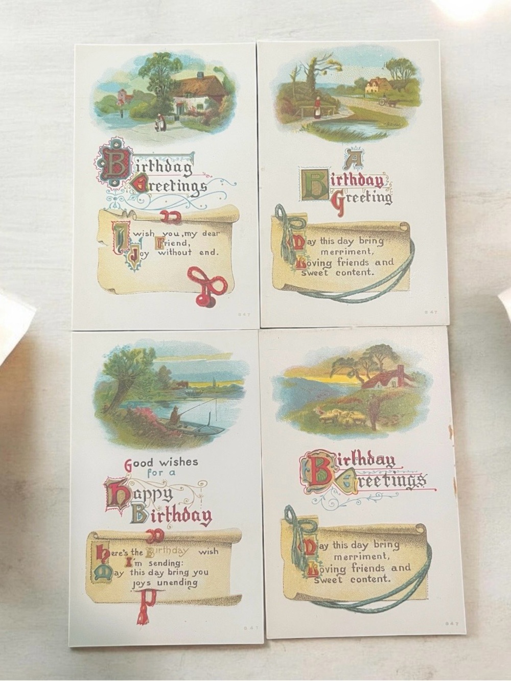 A set of four antique lithographic birthday postcards with pastoral scenes.